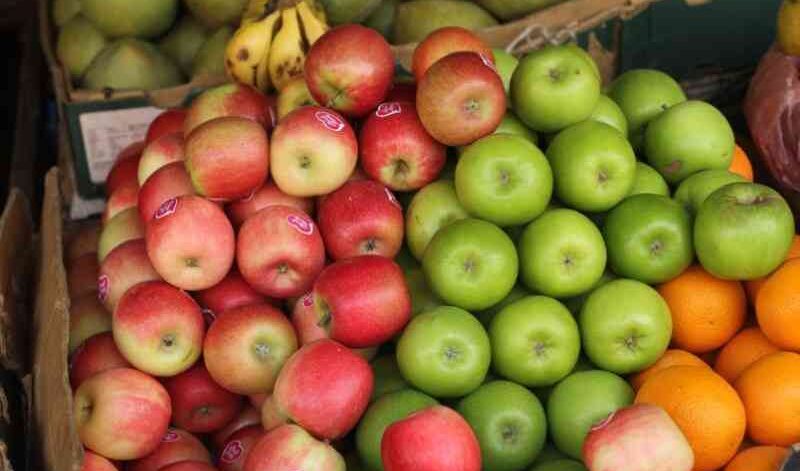 Kenyan fruit vendor arranging imported apples from South Africa showing quality grading and pricing structure at wholesale distribution center